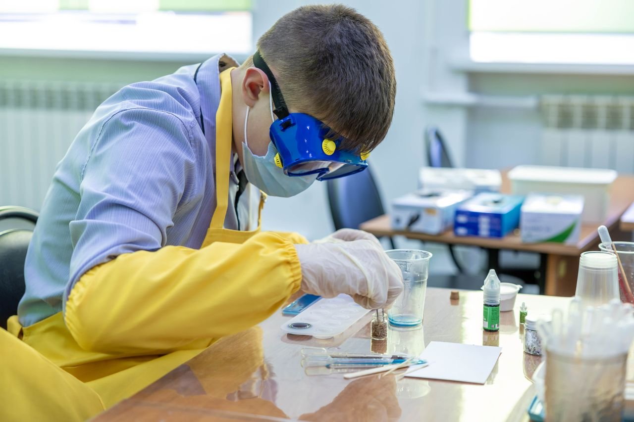 Home Young student in protective gear performing a chemistry experiment in a laboratory setting.